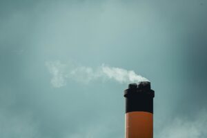Industrial smokestacks emitting carbon emissions into a grey sky, representing compliance carbon markets